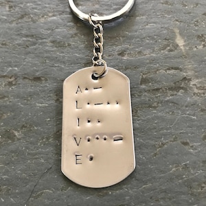 May include: Silver keychain with a dog tag charm engraved with the word "ALIVE" in braille.