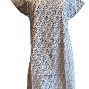 Op de afbeelding: Een knielange jurk met een herhalend donkerblauw en wit paisley-druppelpatroon. Het kledingstuk heeft korte mouwen, een ronde halslijn en een verticale rij kleine witte knoopjes langs de bovenkant van de schouder en borst.