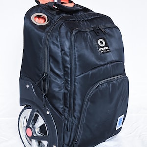 May include: A black rolling backpack with a retractable handle, featuring a Resilience Medical logo patch, multiple zippered compartments, and large wheels with silver spokes and a central pink accent. The interior lining is bright orange.