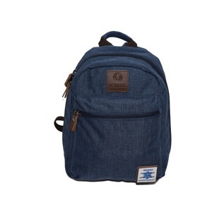 Puede incluir: Una mochila azul marino con un asa superior y dos compartimentos con cremallera. La mochila tiene detalles de cuero marrón en las cremalleras y un parche de cuero marrón con la palabra "RESILIENCE" en la parte delantera. Una pequeña etiqueta blanca con texto en la parte inferior.