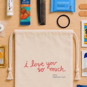Könnte beinhalten: Ein beigefarbener Beutel mit Kordelzug und dem Text i love you so much. K&N FEBRUARY 2025, umgeben von Lippenbalsam, Liquid I.V.-Päckchen, schwarzem Kamm, Abschminktuch, Haargummi, zwei Pflastern, Shout-Tuch, goldenen Augenmasken und einem Minzstick.