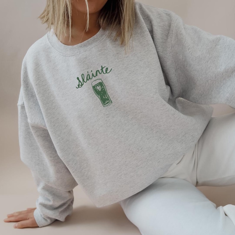 May include: A gray sweatshirt with the Irish phrase "Sl&aacute;inte" and a green illustration of a pint glass of beer.