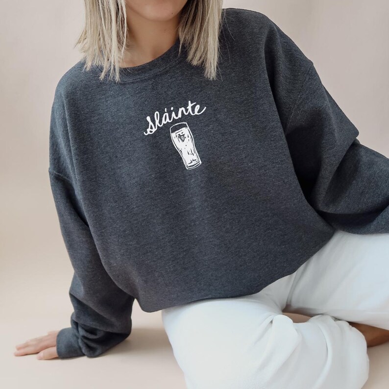 May include: A dark gray cropped sweatshirt with the word "sl&aacute;inte" and a white outline of a pint glass printed on the front.