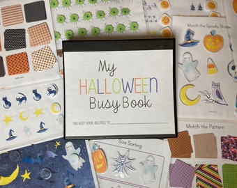 Op de afbeelding: Een zwarte map met de titel "My HALLOWEEN Busy Book" op de omslag. De map is open op een pagina met de titel "Size Sorting" en een afbeelding van een spinnenweb. De map is omringd door verschillende Halloween-stickers.