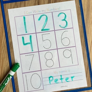 May include: A white sheet of paper with dotted lines for tracing numbers 1 through 10. The numbers are written in green marker. The paper is in a clear plastic frame. The text "I Can Write my Numbers!" is at the top of the page. The text "My name is" is at the bottom of the page. The name "Peter" is written in green marker below the text.