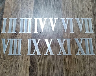 May include: Silver Roman numeral clock numbers, from I to XII, on a wood background.