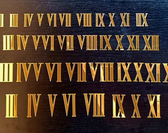 May include: Four rows of gold Roman numeral stickers on a black background. The numerals are I, II, III, IV, V, VI, VII, VIII, IX, X, XI, XII, XIII, and IXXXIXI.
