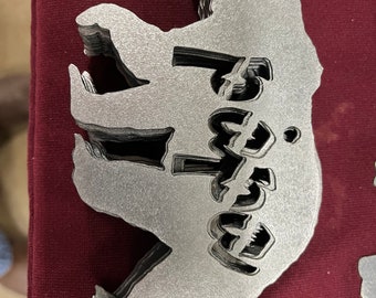 May include: A silver metal bear ornament with the word "Family" cut out in the center. The ornament is stacked on top of other ornaments.