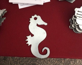 May include: A silver metal seahorse cutout, a popular nautical theme for home decor, is displayed on a red table. The seahorse is a popular choice for coastal and beach-themed home decor.