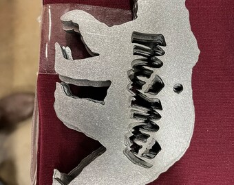 May include: A silver metal bear cutout with the word "Wyoming" cut out inside. The bear is facing left and has a hole at the top for hanging.