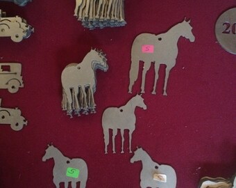 May include: A collection of silver-colored metal horse ornaments and vehicle cutouts on a red surface. The horse ornaments vary in size and are in different poses. Some have price tags attached. The ornaments are likely for crafts or decoration.
