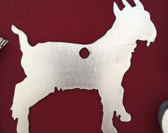 May include: A silver metal cutout of a goat with a hole in the center. The goat is standing on a red surface.