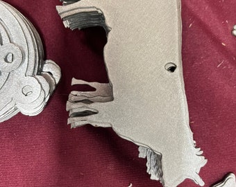 May include: A stack of silver metal cow cutouts. The cutouts are layered on top of each other and have a smooth, metallic finish.