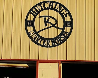 May include: A yellow metal building with a red trim and a black metal sign that says "Houchings Quarter Horses Est. 1999" with a stylized "K" in the center.