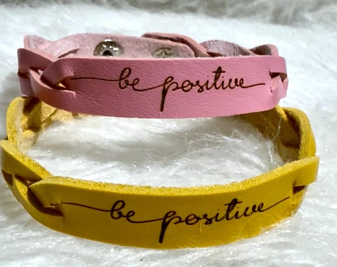 Yellow/purple leather bracelet, featuring the uplifting phrase “be positive” engraved in bold black cursive script
