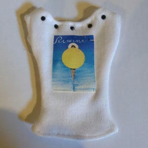 May include: White knitted sock with a label that reads "Rimini" and features a yellow circle over a blue and white background. The sock has a unique shape with small black details.