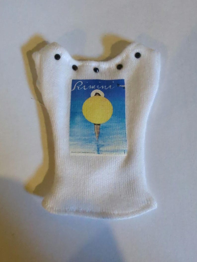 May include: White knitted sock with a label that reads "Rimini" and features a yellow circle over a blue and white background. The sock has a unique shape with small black details.