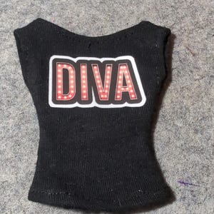 May include: Black sleeveless top with the word "DIVA" in a red and white design. The word "DIVA" is in a bold, stylized font with a light-up effect. The top is made of a soft, dark fabric.