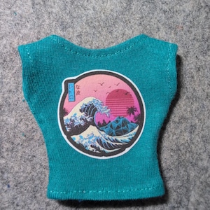 May include: A teal sleeveless shirt featuring a circular graphic print on the front. The design depicts a stylized ocean wave, a pink sunset, palm trees, and a geometric mountain. Japanese text is visible in a blue box on the left side.