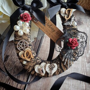 Può includere: Due ornamenti decorativi a forma di ferro di cavallo. Ogni ferro di cavallo è avvolto in materiale marrone strutturato e adornato con fiocchi neri, pizzo, perle finte e rose rosse. Uno ha un ciondolo a pentagramma e l'altro un ciondolo a pipistrello. L'etichetta recita "Wishing Well Handmade Gifts & Decor."
