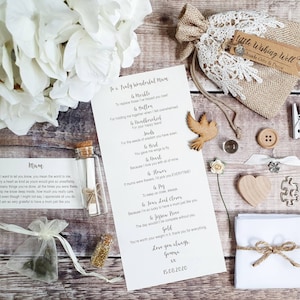 May include: A white card with a handwritten message to a mother, with the text "To a truly wonderful Mum" and a list of items, including a marble, a button, a hand-drawn bird, seeds, a heart, a flower, a key, a four-leaf clover, a jigsaw piece, and gold. The card is surrounded by a variety of small items, including a small glass bottle, a small bag of gold glitter, a small white bag, a small wooden heart, a small wooden button, a small wooden bird, a small white clothespin, and a small white piece of paper.