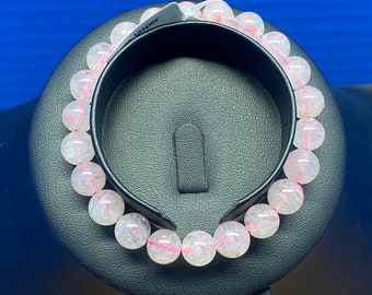 May include: A pink jasper bracelet with a white background. The bracelet is made of round beads with a light pink color and white streaks.