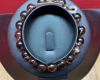 May include: A brown gemstone bracelet with a silver clasp. The bracelet is made of round beads and is displayed on a black stand.