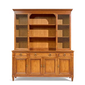 May include: A wooden hutch with a light brown finish. The top section has two mesh-covered doors and open shelves. The bottom section features drawers and cabinet doors with ring pulls and brass hardware. The hutch is a classic furniture piece.