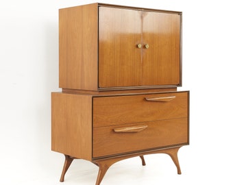 Puede incluir: Un armario de madera de estilo moderno de mediados de siglo con dos puertas y dos cajones. El armario tiene un acabado de madera clara y cuenta con herrajes de latón. El armario está sobre cuatro patas anguladas.