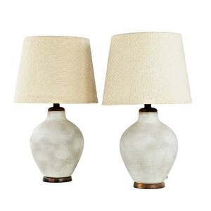 May include: A pair of white ceramic table lamps with off-white fabric lampshades. The lamps have a textured, distressed finish.