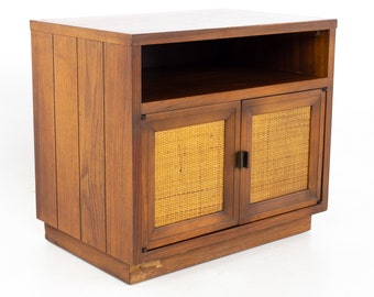 May include: A mid-century modern wooden cabinet with two doors. The doors are made of woven cane and have brass hardware. The cabinet has a shelf and a base.
