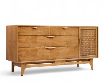 May include: A mid-century modern wooden dresser with four drawers and a woven panel door. The dresser is made of light-colored wood and has a curved base and angled legs. The drawers have curved wooden handles.