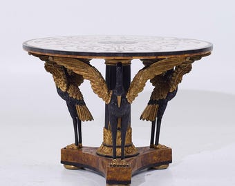 May include: A round, black and gold table with a marble top. The table has three legs that are shaped like cranes with outstretched wings.