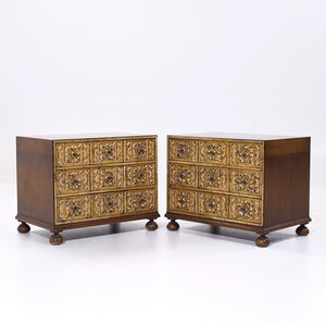 May include: Two wooden chest of drawers with intricate carved details in gold paint. The chests have three drawers each and stand on four legs.