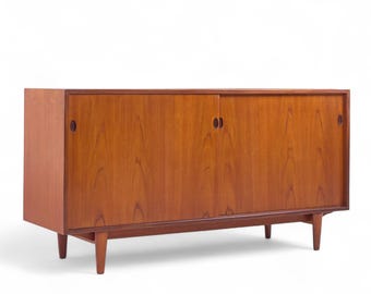 May include: A mid-century modern wooden cabinet with a warm, reddish-brown finish. The cabinet features sliding doors and a low profile, supported by tapered legs. The design is simple and elegant, suitable for storage.