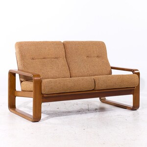 May include: A brown two-seater sofa with a light brown fabric upholstery. The sofa has a simple, mid-century modern design with curved wooden arms and legs.