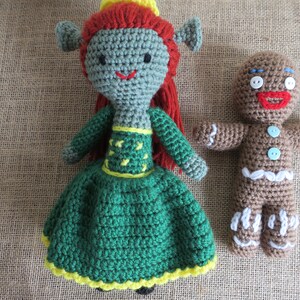 May include: Two crocheted stuffed toys. A green and yellow princess doll with red hair and a brown gingerbread man with white icing.