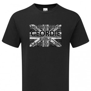 May include: Black t-shirt with a distressed Union Jack graphic and text that reads "BRITISH BY BIRTH GEORDIE BY THE GRACE OF GOD". The shirt is a crew neck style.