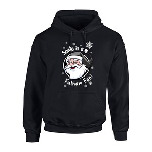 May include: Black hooded sweatshirt with a white graphic of Santa Claus wearing a Fulham Football Club jersey and the text "Santa is a Fulham Fan!" with snowflakes surrounding the graphic.