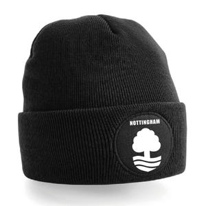 Könnte beinhalten: Schwarze Mütze mit einem weißen runden Aufnäher mit dem Logo des Nottingham Forest Football Clubs. Das Logo ist ein weißer Baum mit einem weißen Fluss und dem Wort "NOTTINGHAM" über dem Baum.