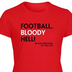 May include: A red t-shirt with the text "FOOTBALL, BLOODY HELL!" in black and white. Below the text is "SIR ALEX FERGUSON 26th MAY 1999". The shirt has short sleeves and a crew neck.