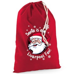 May include: A red drawstring gift bag with the text "Santa is a Liverpool Fan!" and a cartoon image of Santa Claus. The bag has a white drawstring closure and white snowflakes around the Santa image.