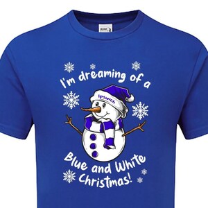 May include: Royal blue t-shirt featuring a snowman graphic with a carrot nose, wearing a blue and white scarf and hat. The text reads "I'm dreaming of a Blue and White Christmas!" with snowflakes.