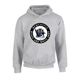 Pu&ograve; includere: Una felpa con cappuccio grigia con un logo circolare bianco e nero che presenta un castello, una gazza e il testo "Newcastle Black and White Army".