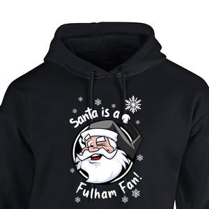 May include: Black hooded sweatshirt with a white graphic of Santa Claus wearing a black and white hat and a white beard. The graphic says "Santa is a Fulham Fan!" with snowflakes around the graphic.