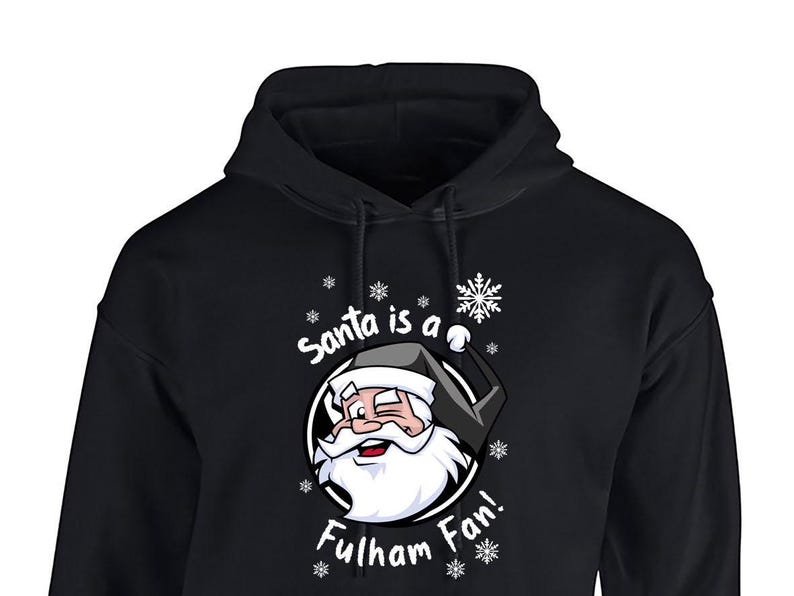 May include: Black hooded sweatshirt with a white graphic of Santa Claus wearing a black and white hat and a white beard. The graphic says "Santa is a Fulham Fan!" with snowflakes around the graphic.