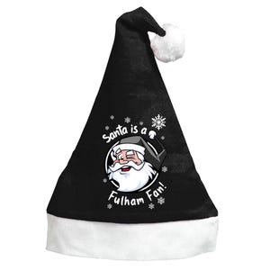 Op de afbeelding: Zwarte kerstmuts met een witte rand en een witte pompon. De hoed heeft een afbeelding van de kerstman met de tekst "Santa is a Fulham Fan!" in het wit. Sneeuwvlokken zijn verspreid rond de tekst en de kerstman-afbeelding.