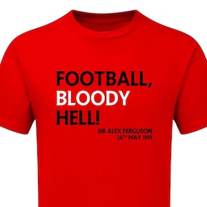 May include: A red t-shirt with the text "FOOTBALL, BLOODY HELL!" in black and white. Below the text is "SIR ALEX FERGUSON 26TH MAY 1999" in black. The shirt is a crew neck style.