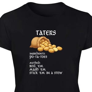 Op de afbeelding: Zwart T-shirt met een afbeelding van een jute zak met aardappelen en het woord "TATERS" erboven. De tekst eronder geeft ingrediënten en kookmethoden weer: "po-ta-toes", "BOIL 'EM", "MASH 'EM", "STICK 'EM IN A STEW".