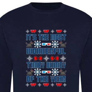 May include: Navy blue sweatshirt with a festive design. The text reads "IT'S THE MOST WONDERFUL TIMEY WIMEY OF THE YEAR" in a pixelated font, with hearts, snowflakes, and 3D glasses graphics. A fun, holiday-themed sweater.